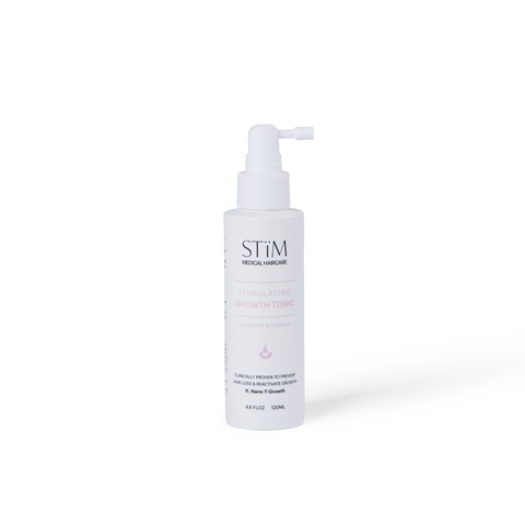 Stïm Haircare stimulating growth tonic bottle with label, clear liquid inside, on a neutral background.