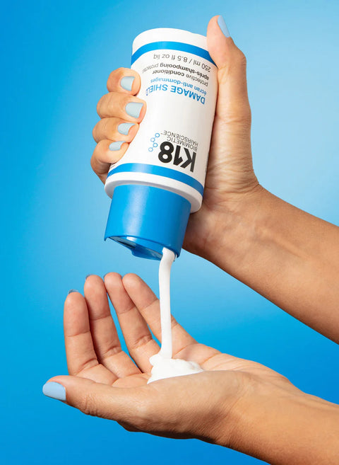 K18 Damage Shield Protective Conditioner in 8.5 oz bottle, showing the conditioner tube held in hand with product branding visible.