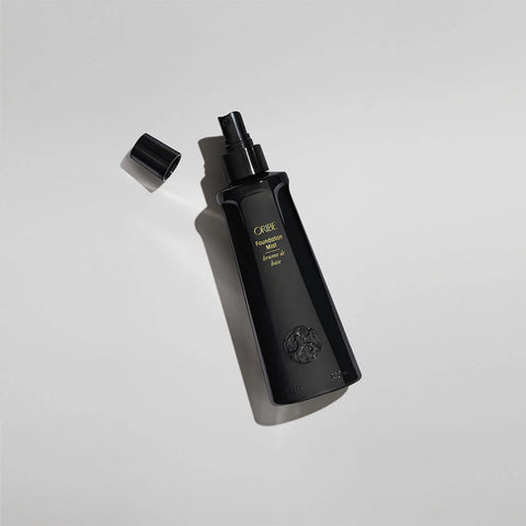 Oribe Foundation Mist styling spray bottle with a sleek black design and gold accents, shown on a neutral background.