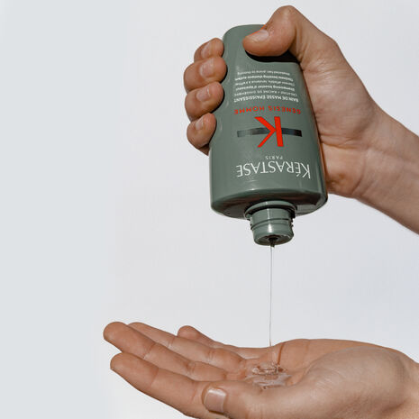 Kérastase Genesis Homme Bain de Masse thickening shampoo for men held in hand, showing the 250ml bottle with branding.
